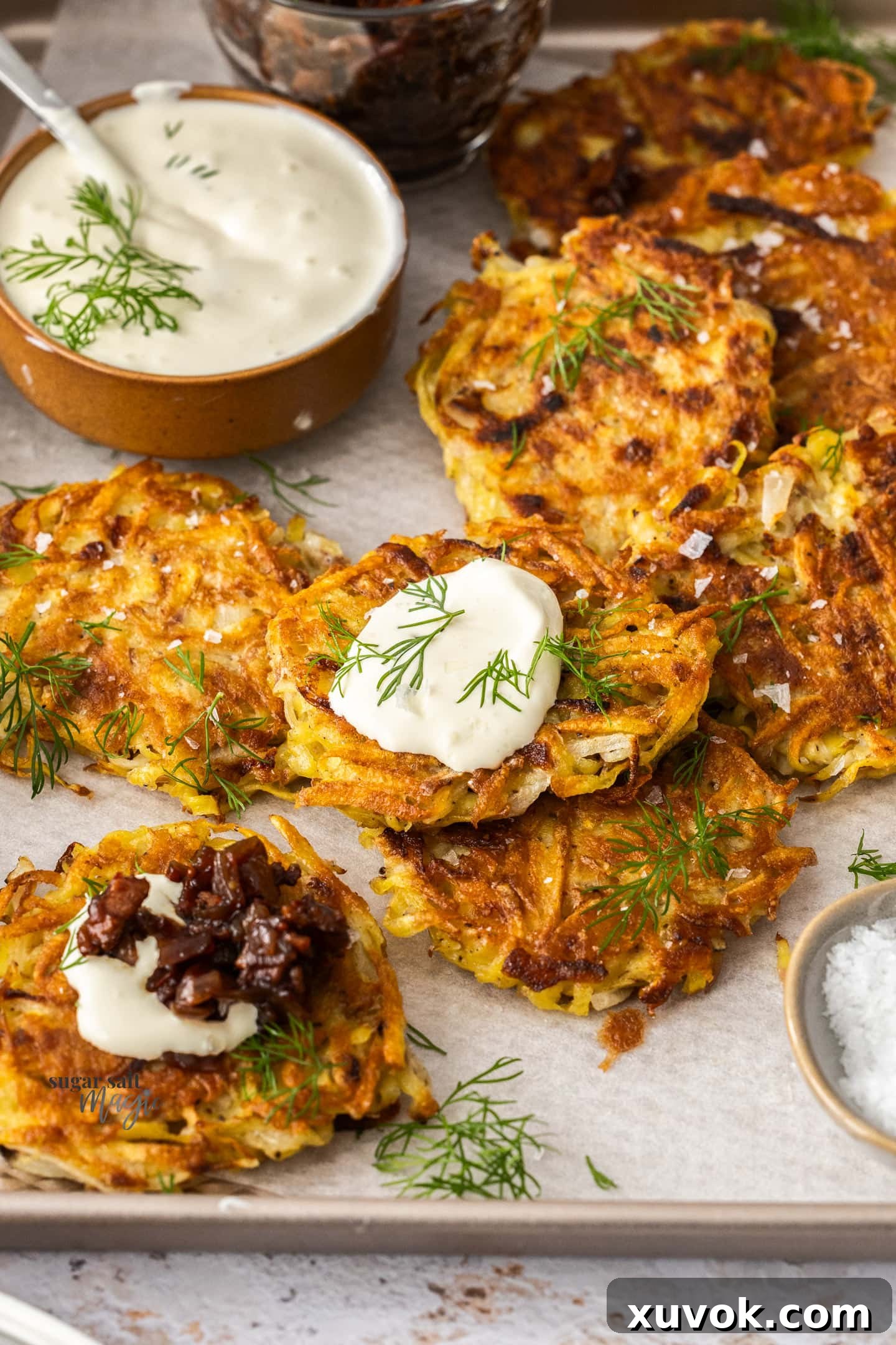 Golden potato fritters on a baking tray, one generously topped with a dollop of creamy sour cream and fresh chives.