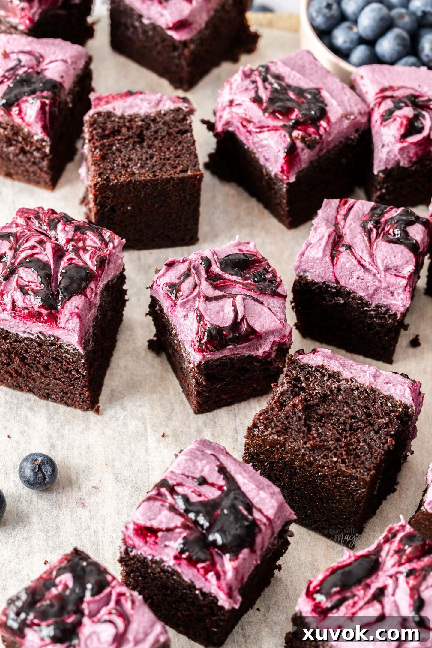 Square slices of blueberry chocolate cake on a wooden board, showing the even layers of cake and frosting.