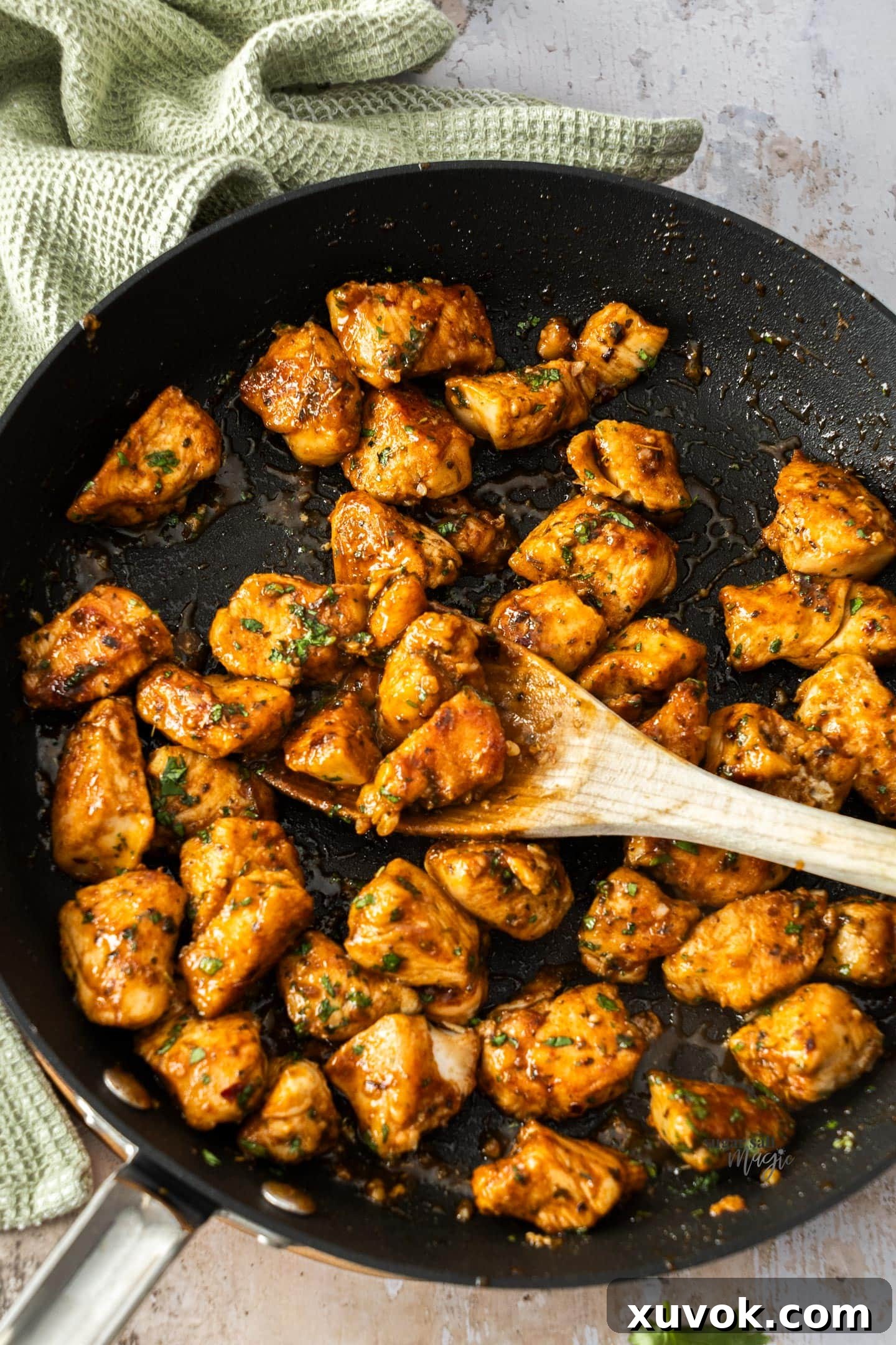 A glistening skillet filled with golden brown spicy chicken bites, garnished with fresh herbs, ready to be served.
