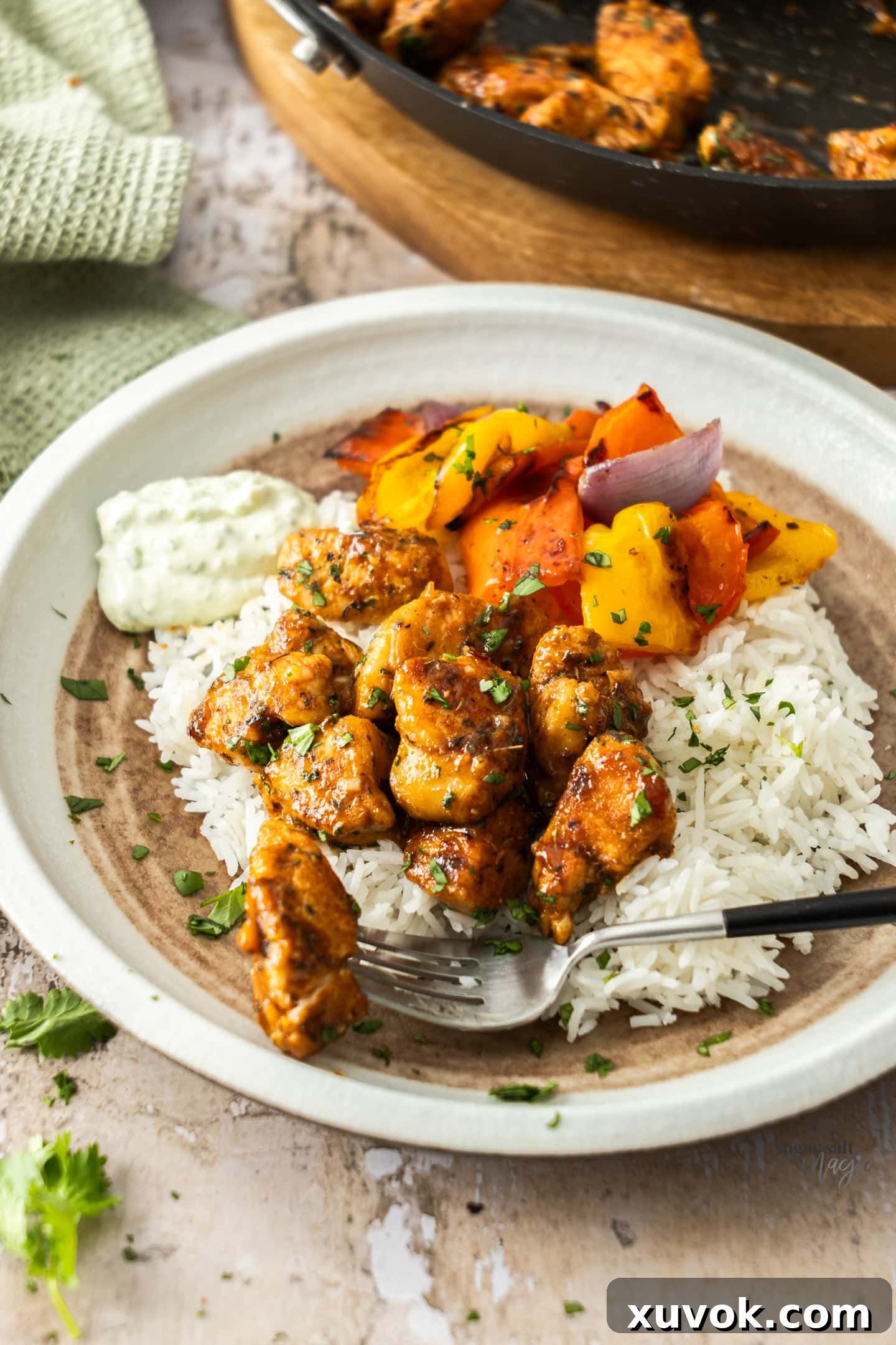 A plate of spicy chicken bites served alongside fluffy white rice and vibrant roasted bell peppers, creating a complete meal.