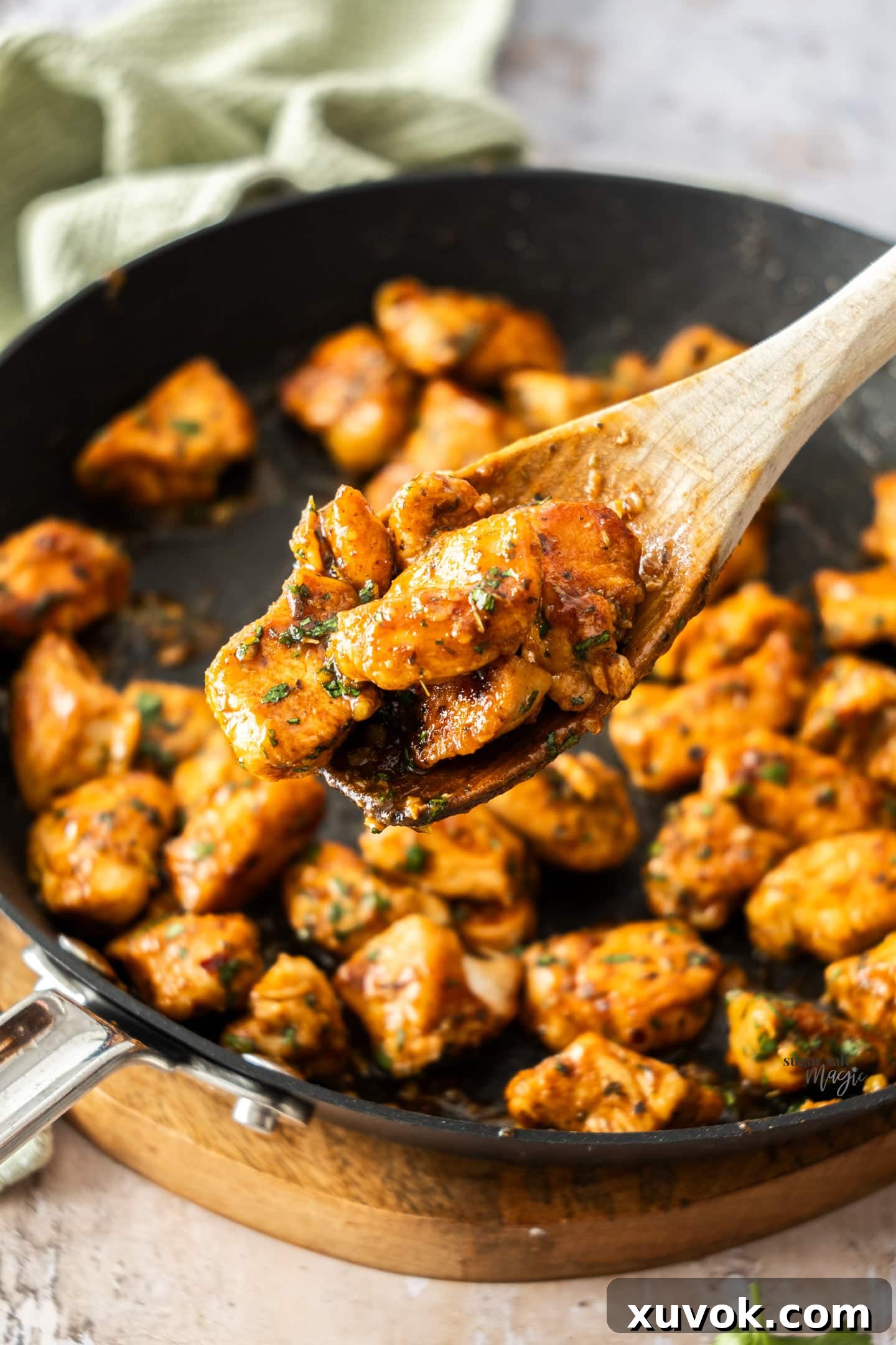 A close-up shot of several spicy chicken bites resting on a wooden spoon, showcasing their sticky glaze and fresh herb garnish.