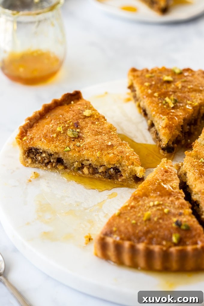 Three perfectly cut slices of Honey Baklava Tart elegantly arranged on a marble cake plate, with a small pot of golden syrup positioned invitingly behind them.