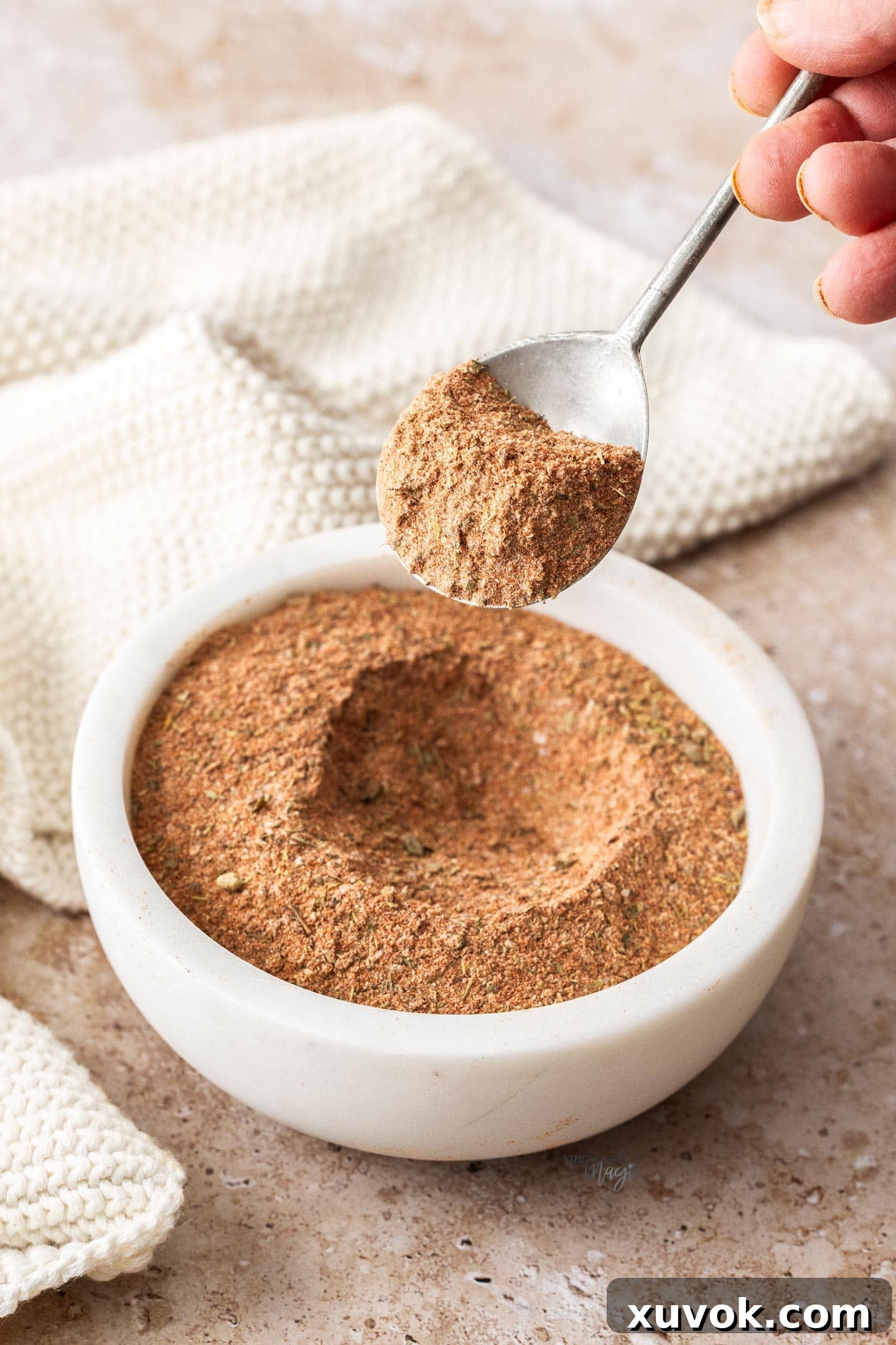 A spoon taking Cajun spice mix out of a bowl, showcasing its rich texture.