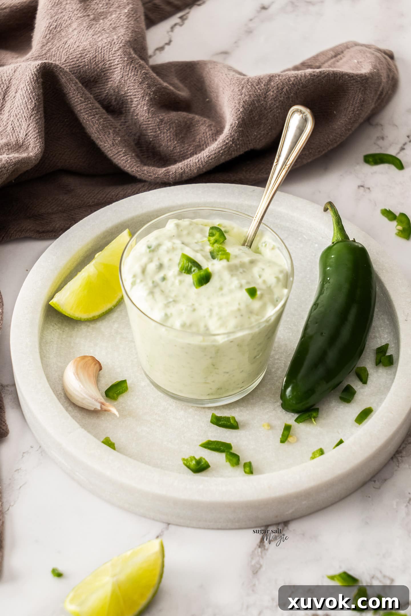 A glass of jalapeno mayo on a marble dish, garnished with fresh jalapeno slices.