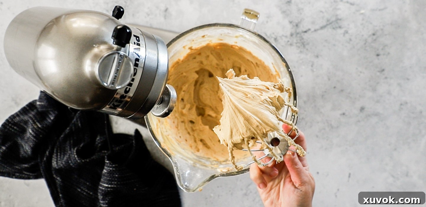 A hand holding a whisk with coffee buttercream.