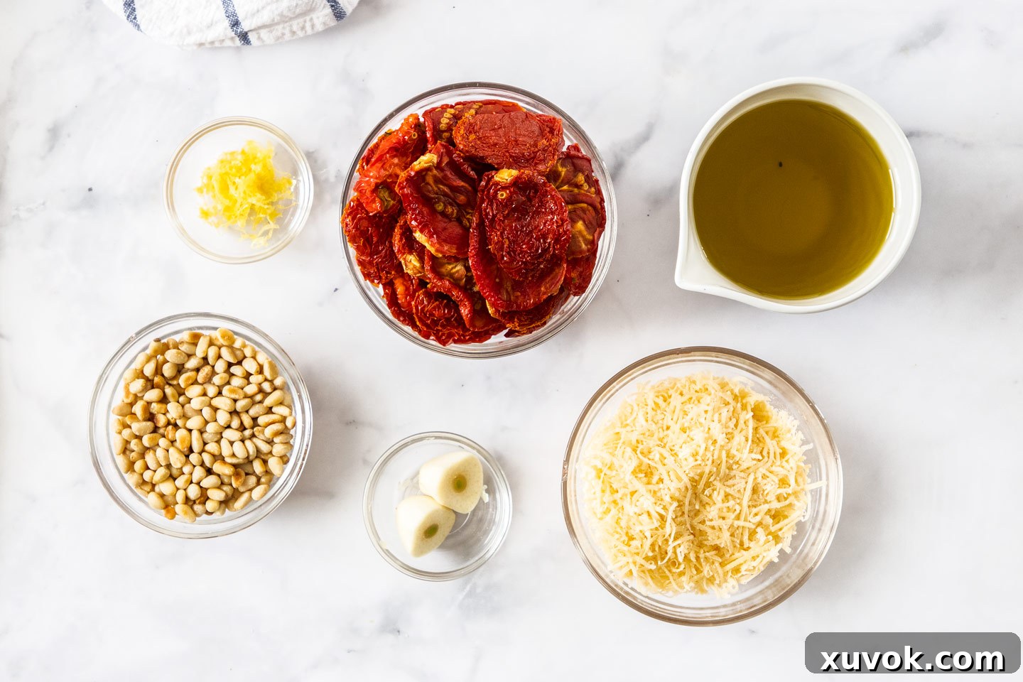 Ingredients for homemade sundried tomato pesto laid out on a marble surface.