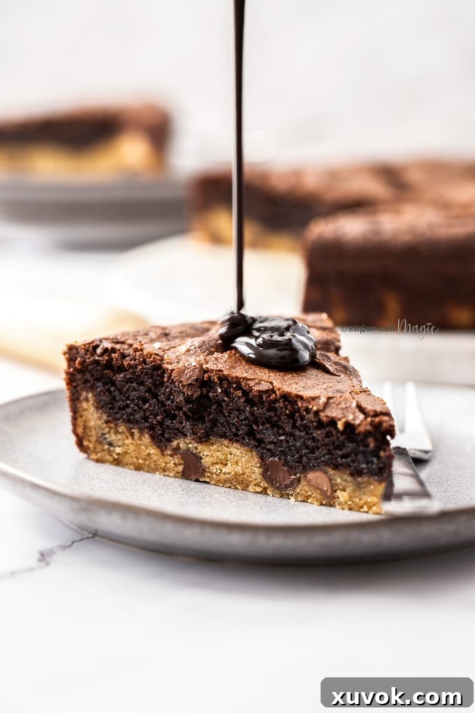 A slice of brownie pie on a grey plate with chocolate sauce being poured on top.