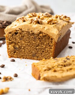 A beautifully sliced coffee and walnut loaf cake, revealing its moist interior and creamy frosting, with a piece cut out, ready to be served.