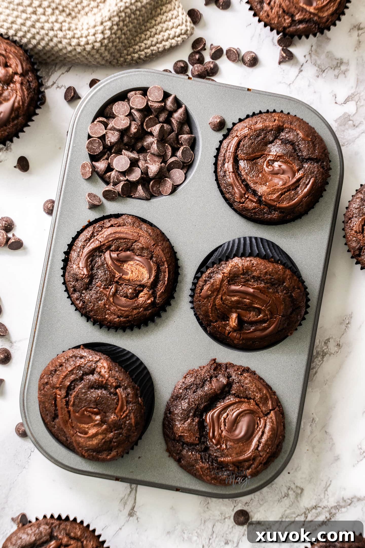 Top down view of 5 fluffy triple chocolate muffins in a muffin tin, showcasing their signature cracked tops and rich brown color.