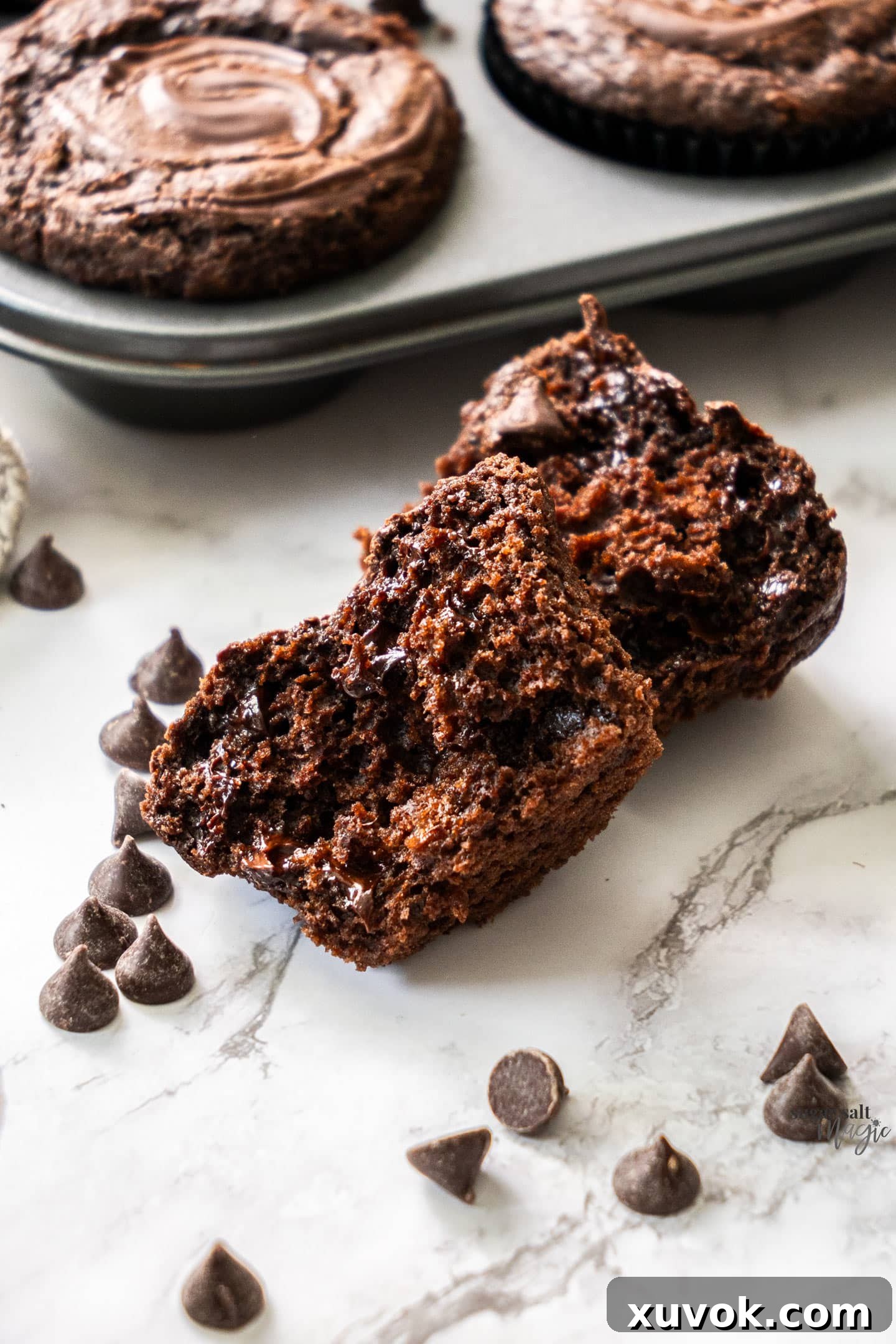 A close-up shot of a triple chocolate muffin broken in half, revealing its moist, tender crumb packed with melted chocolate chips, indicating its rich and indulgent interior.
