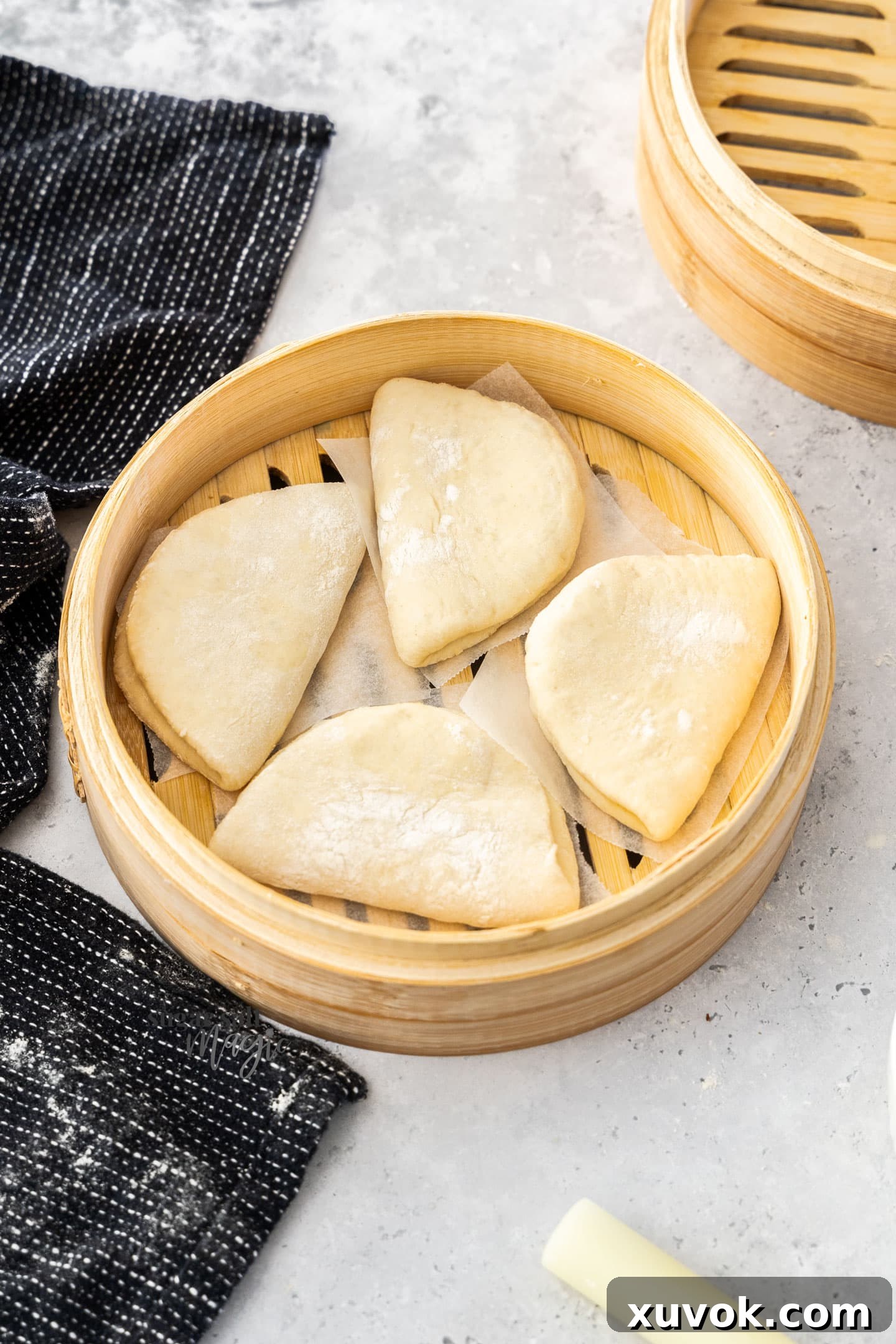 4 uncooked bao buns in a bamboo steamer.