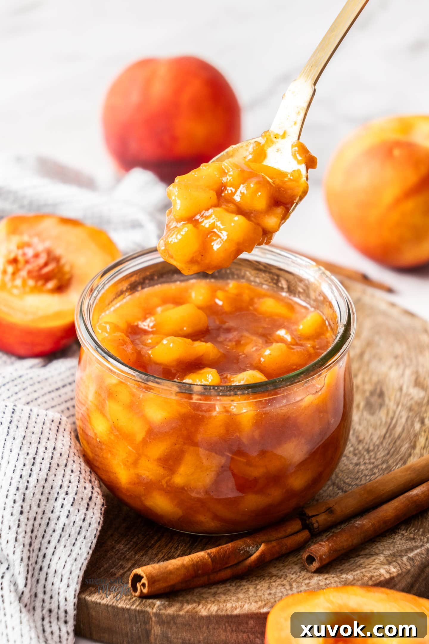 A spoon scooping a generous portion of peach compote from a glass jar, highlighting its luscious texture.