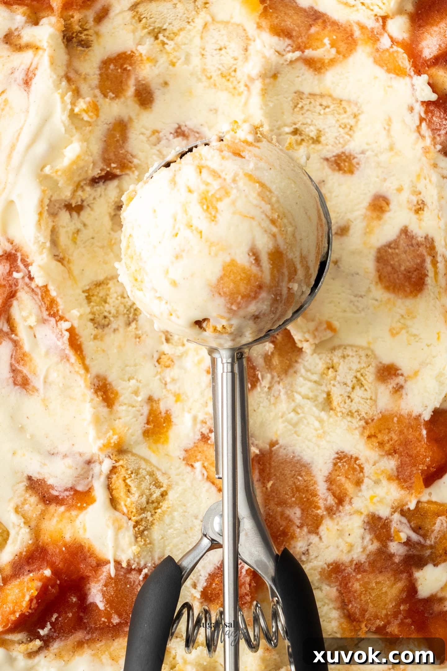An ice cream scoop with a scoop of peach cobbler ice cream, showcasing the creamy texture and embedded cobbler pieces.