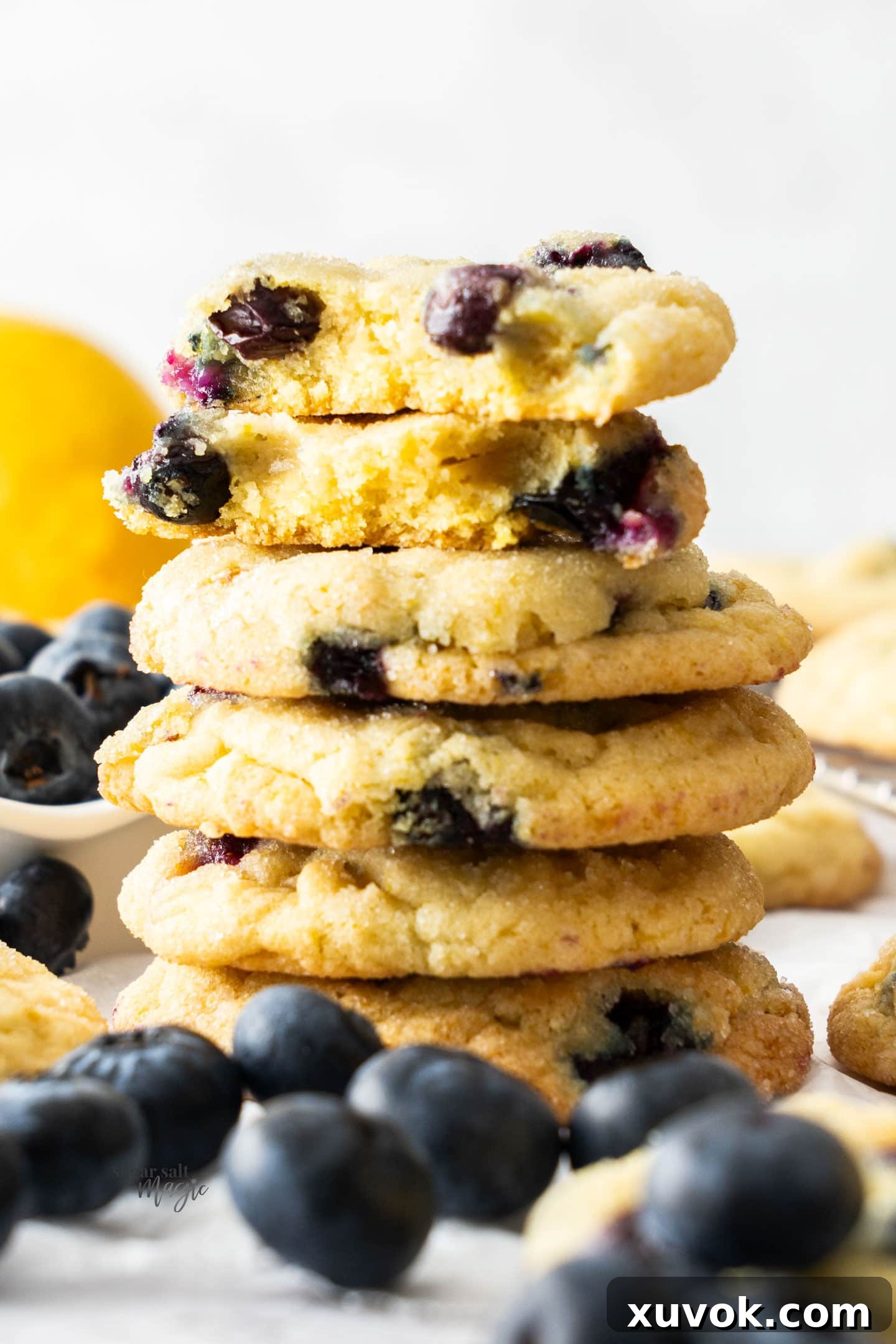 A stack of lemon blueberry cookies, the top one broken in half to show the soft interior.