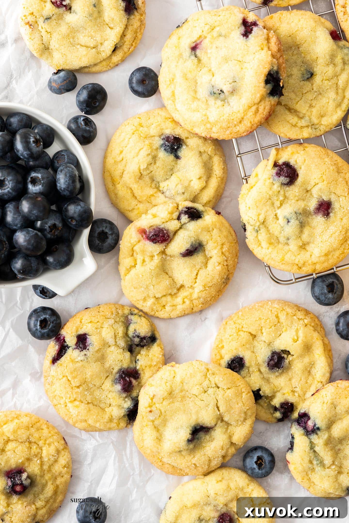 A batch of baked lemon blueberry cookies on a sheet of baking paper.