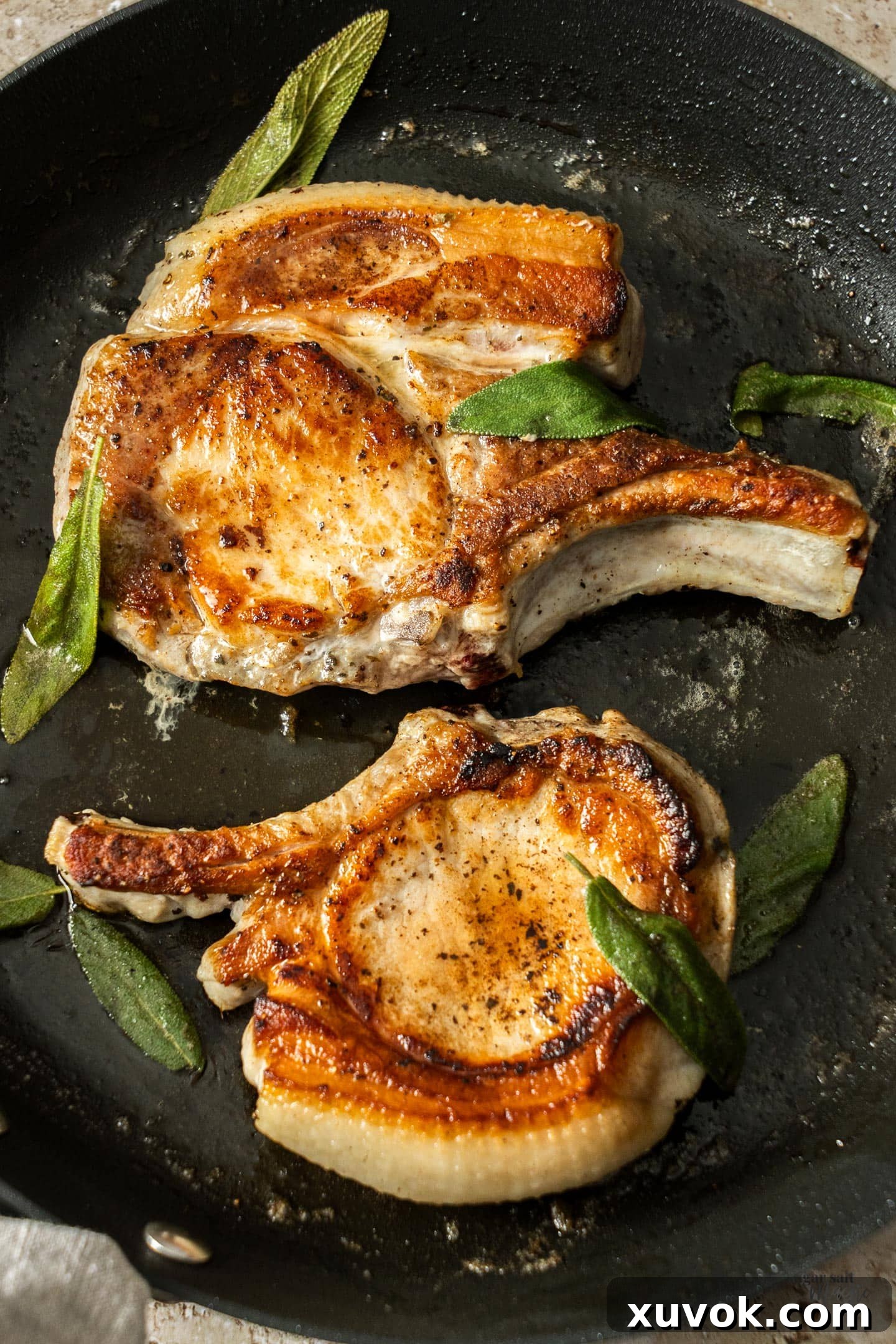 Two perfectly cooked, golden-brown pork chops resting in a skillet, ready to be served, showcasing their juicy texture.