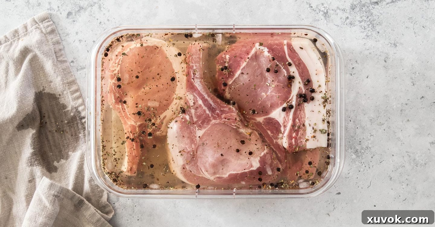 Raw pork chops soaking in a transparent brine solution within a glass container, ready for absorption.