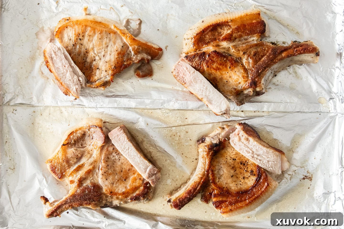 Four golden-brown baked pork chops arranged on a baking sheet, showcasing different levels of doneness and sear.