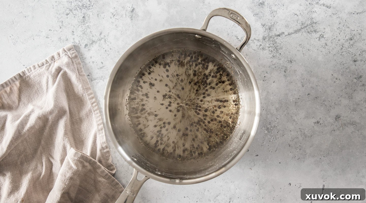 Whole black peppercorns and dried sage leaves added to the hot water in a saucepan, infusing their flavors.