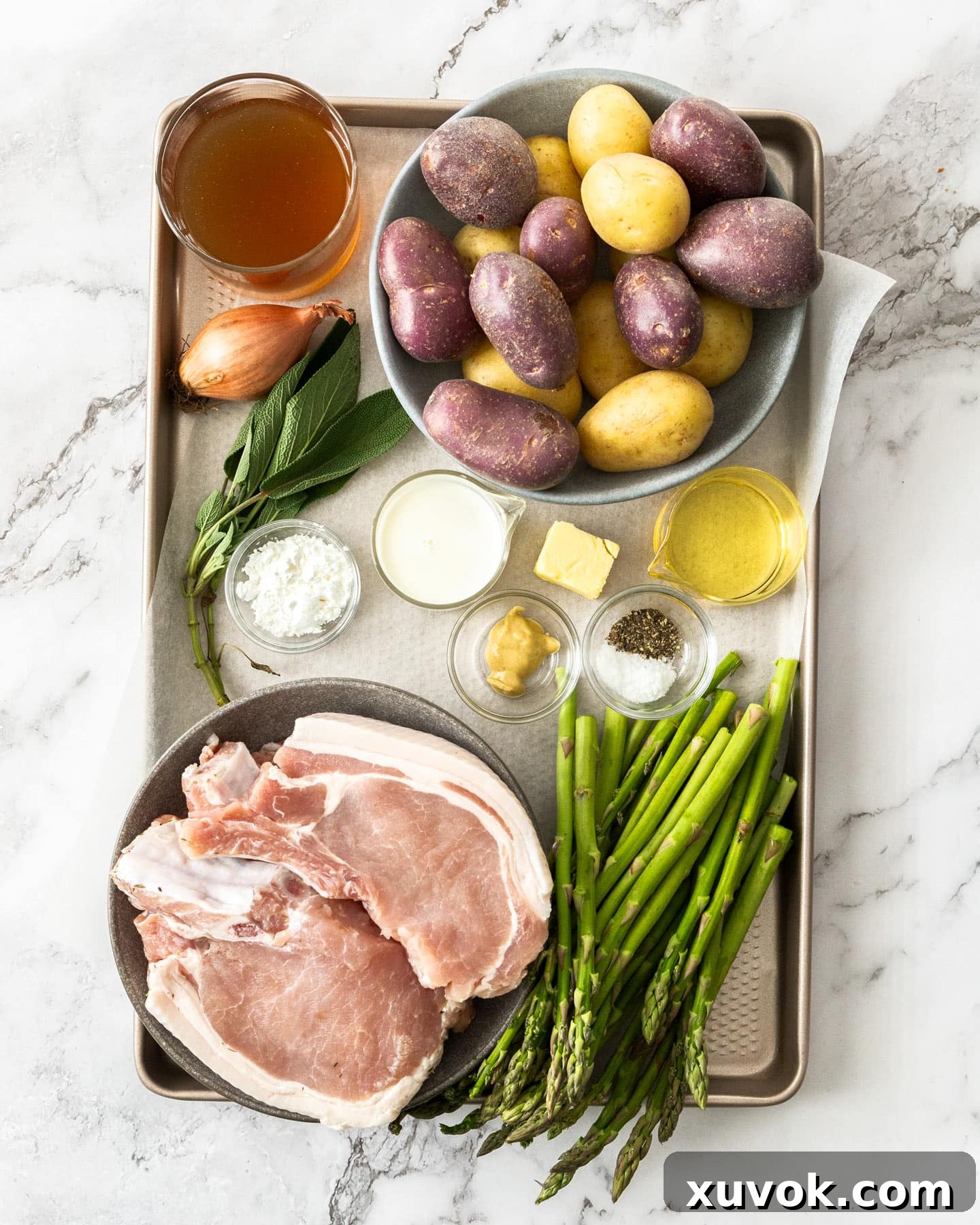 Ingredients for oven baked pork chops and potatoes on a baking tray, neatly arranged.