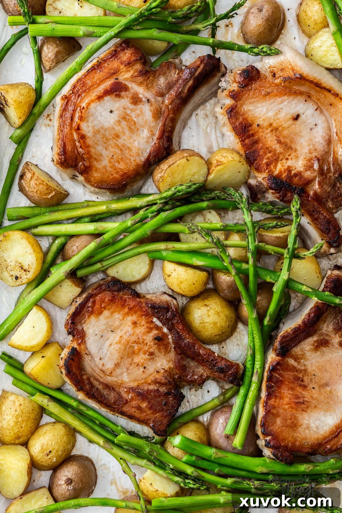 Four perfectly cooked pork chops with roasted potatoes and asparagus on a baking tray, ready to serve.