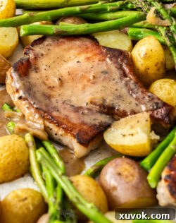A pork chop with potatoes and asparagus with sauce on top.