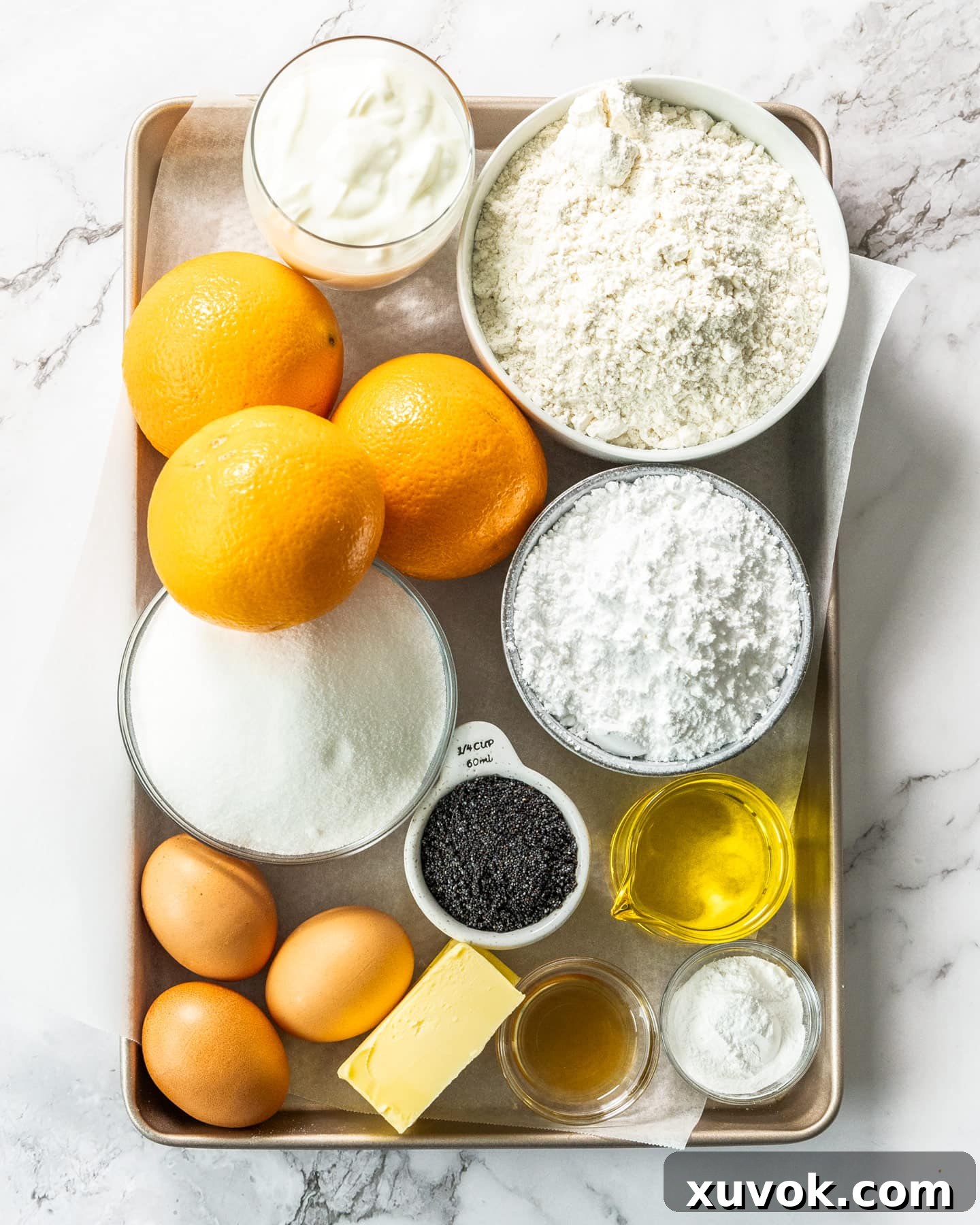 Fresh ingredients for orange and poppy seed cake laid out on a baking tray, including oranges, eggs, butter, flour, and a bowl of poppy seeds.