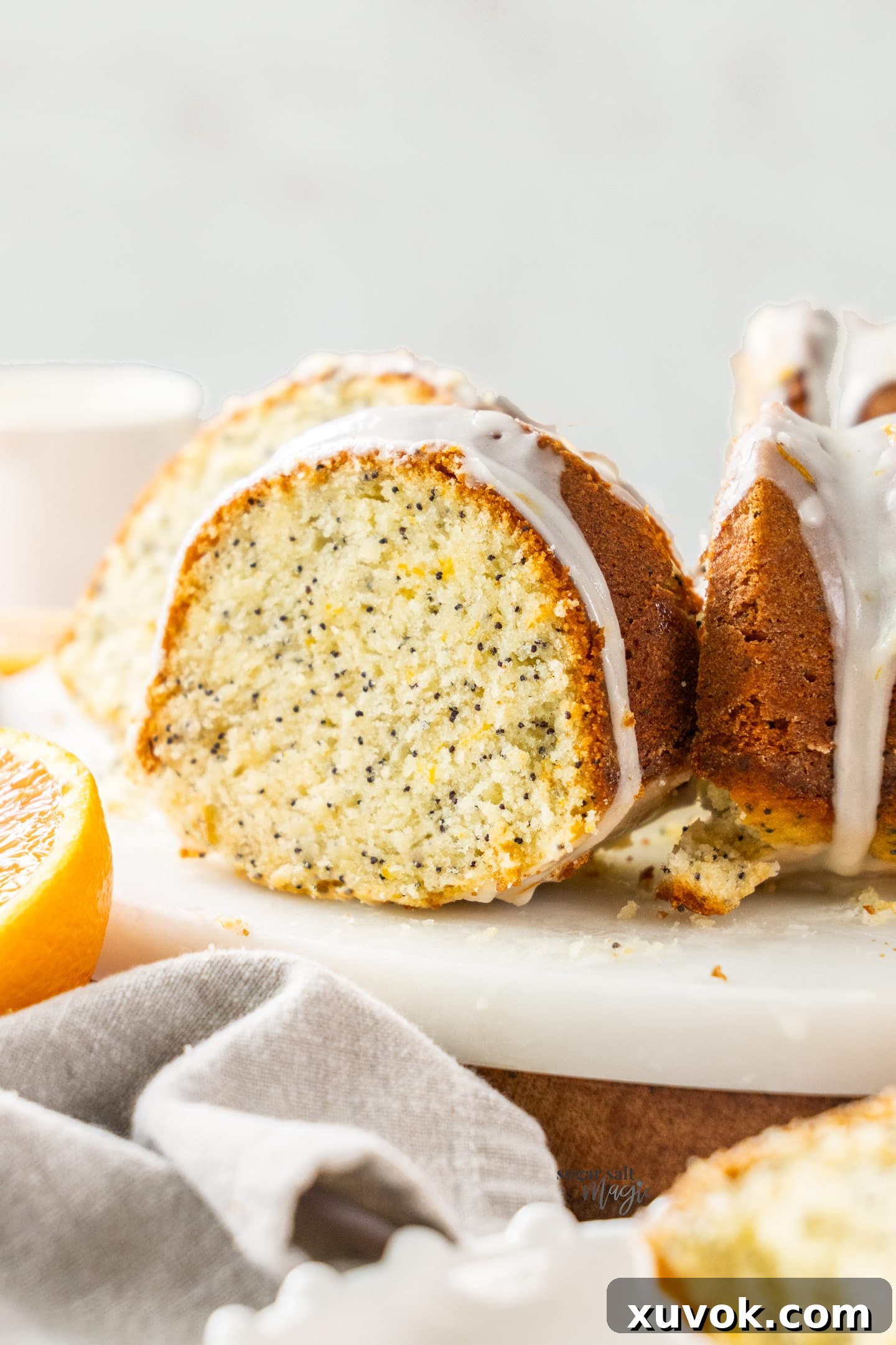 A vibrant slice of orange and poppy seed bundt cake on a marble platter, showcasing its moist texture and poppy seed flecks.