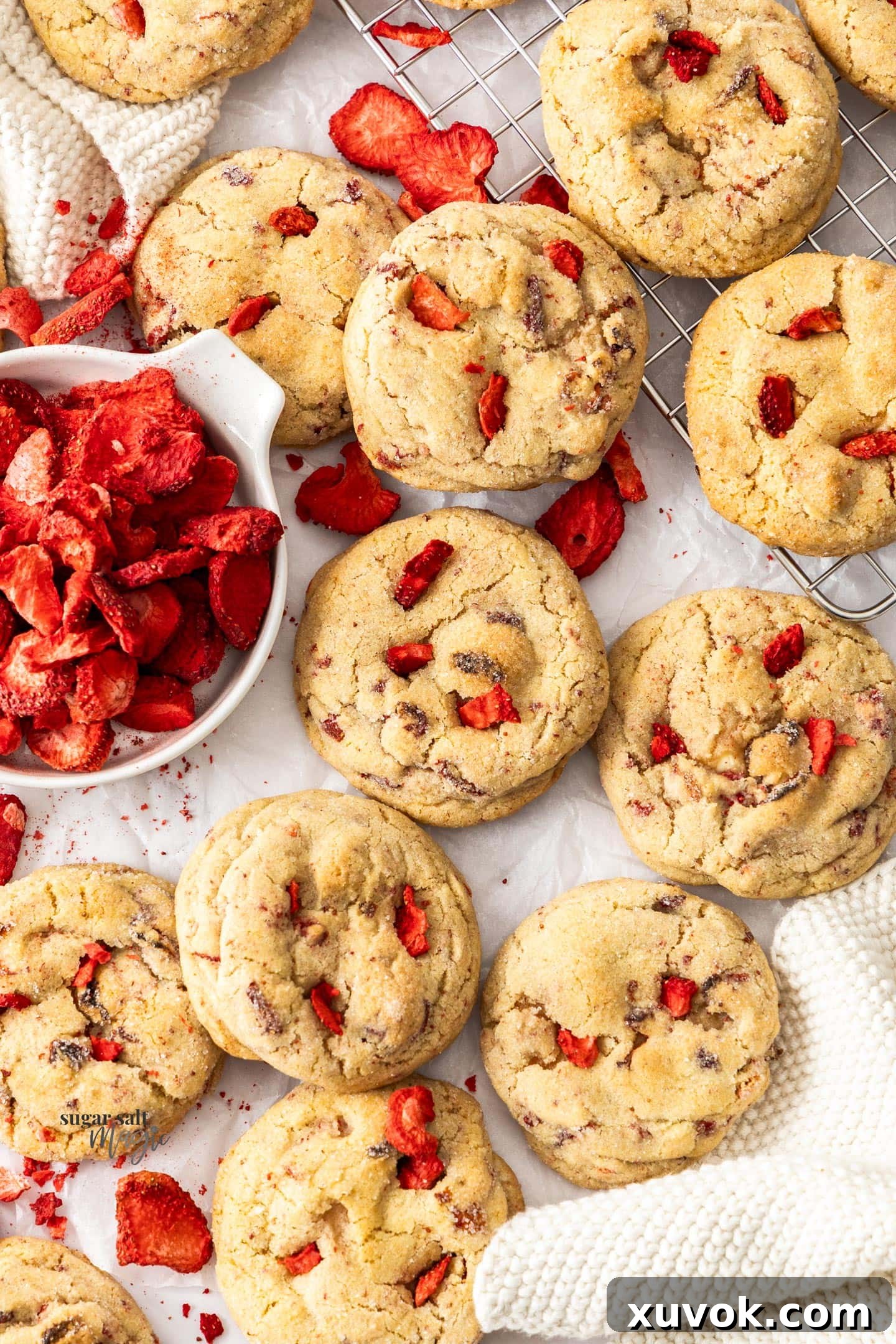A batch of cheesecake stuffed cookies surrounded by freeze dried strawberries. These strawberry cheesecake cookies are buttery, thick, soft, and creamy all in one bite with crisp edges. The gorgeous cookies are spiked with real strawberry pieces and a rich cheesecake centre!