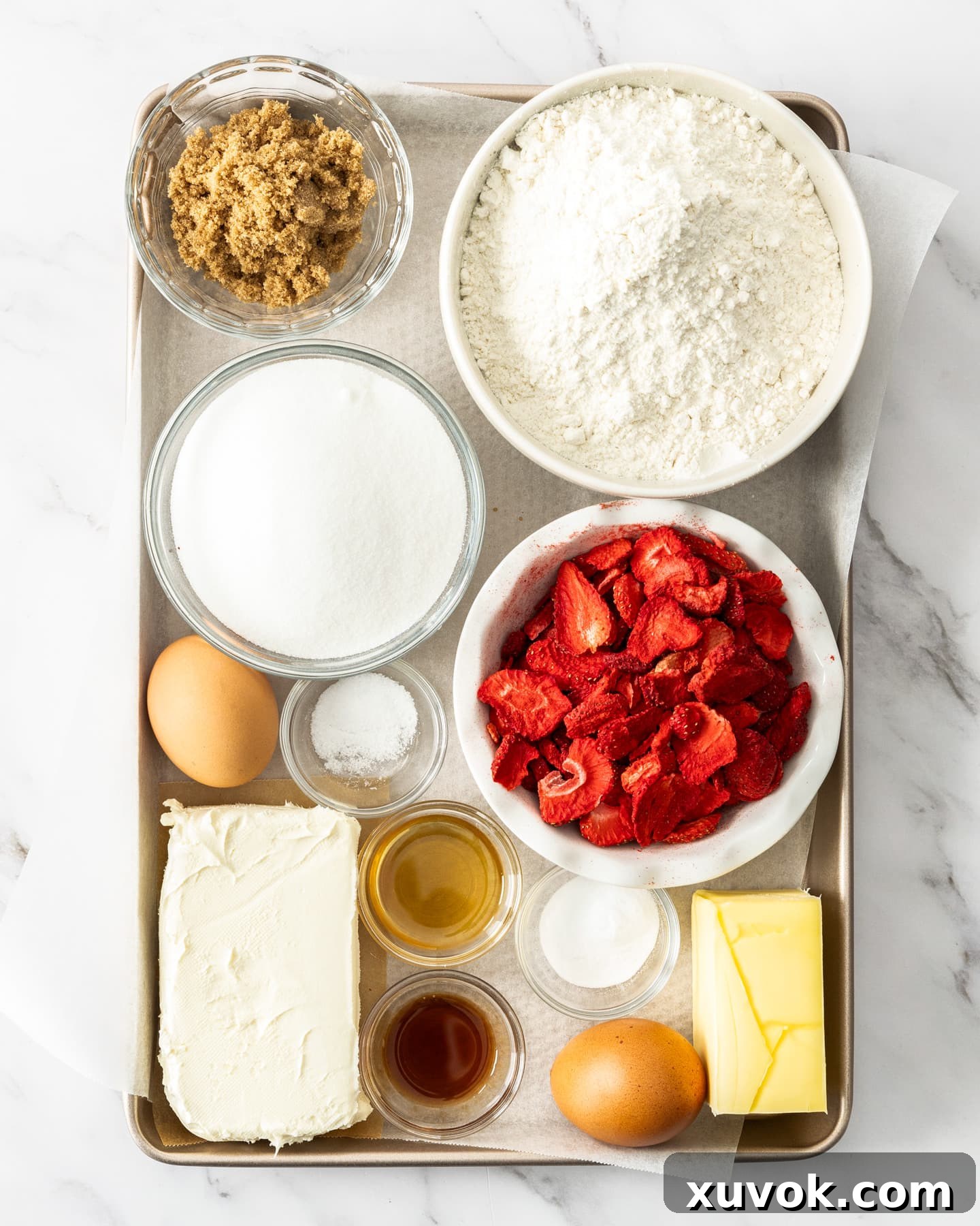 Ingredients for strawberry cheesecake cookies on a baking tray. These strawberry cheesecake cookies are buttery, thick, soft, and creamy all in one bite with crisp edges. The gorgeous cookies are spiked with real strawberry pieces and a rich cheesecake centre!