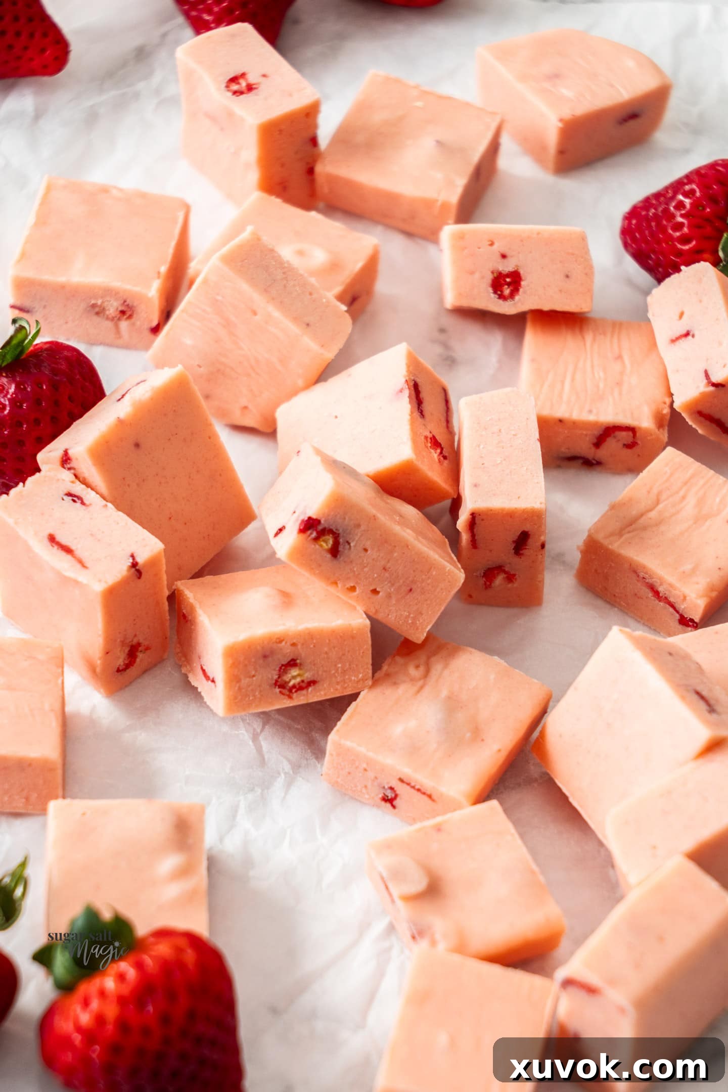 Perfectly cut squares of vibrant pink strawberry fudge arranged neatly on a sheet of baking paper.