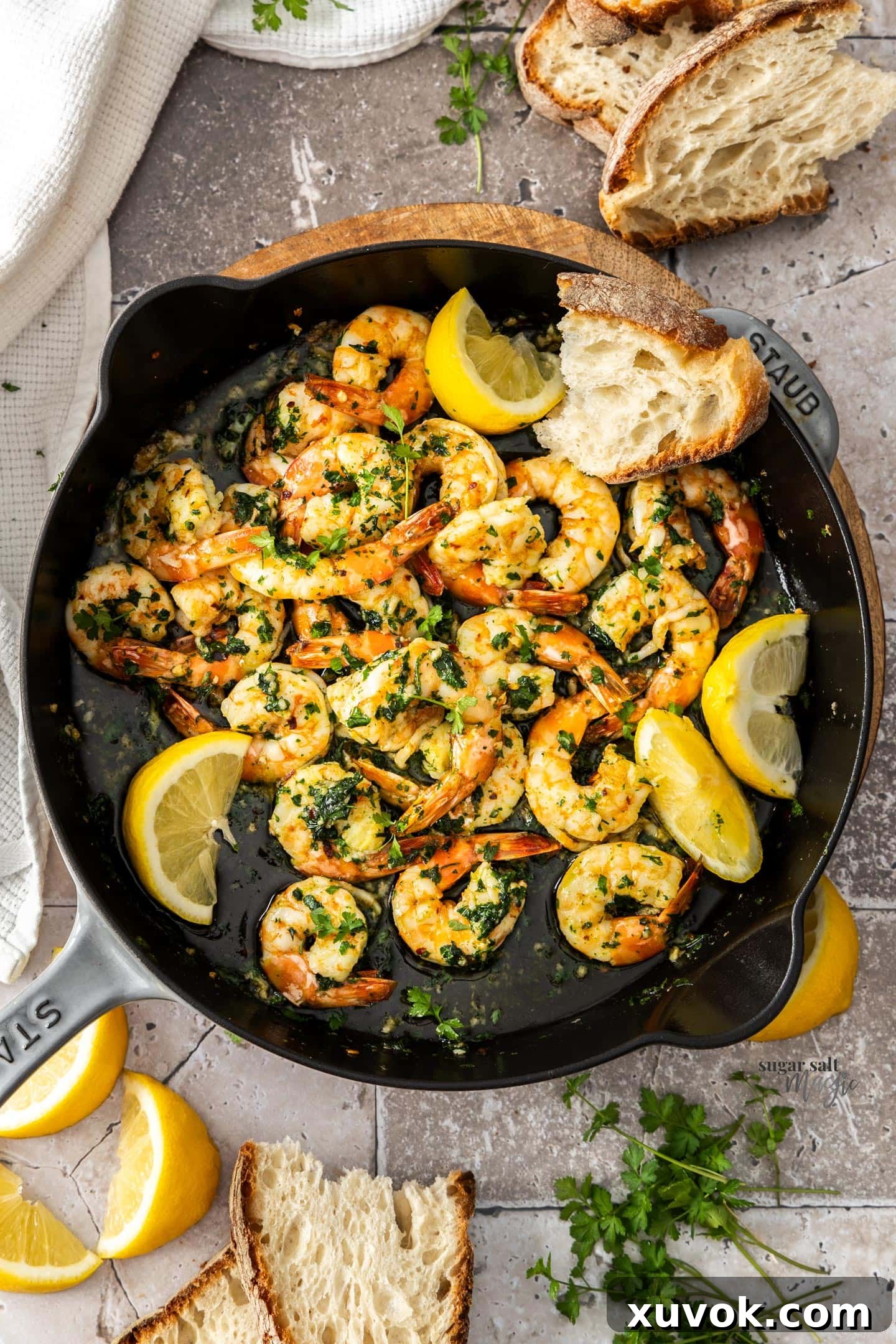 Top down view of a pan full of sizzling garlic prawns, garnished with parsley and lemon wedges.