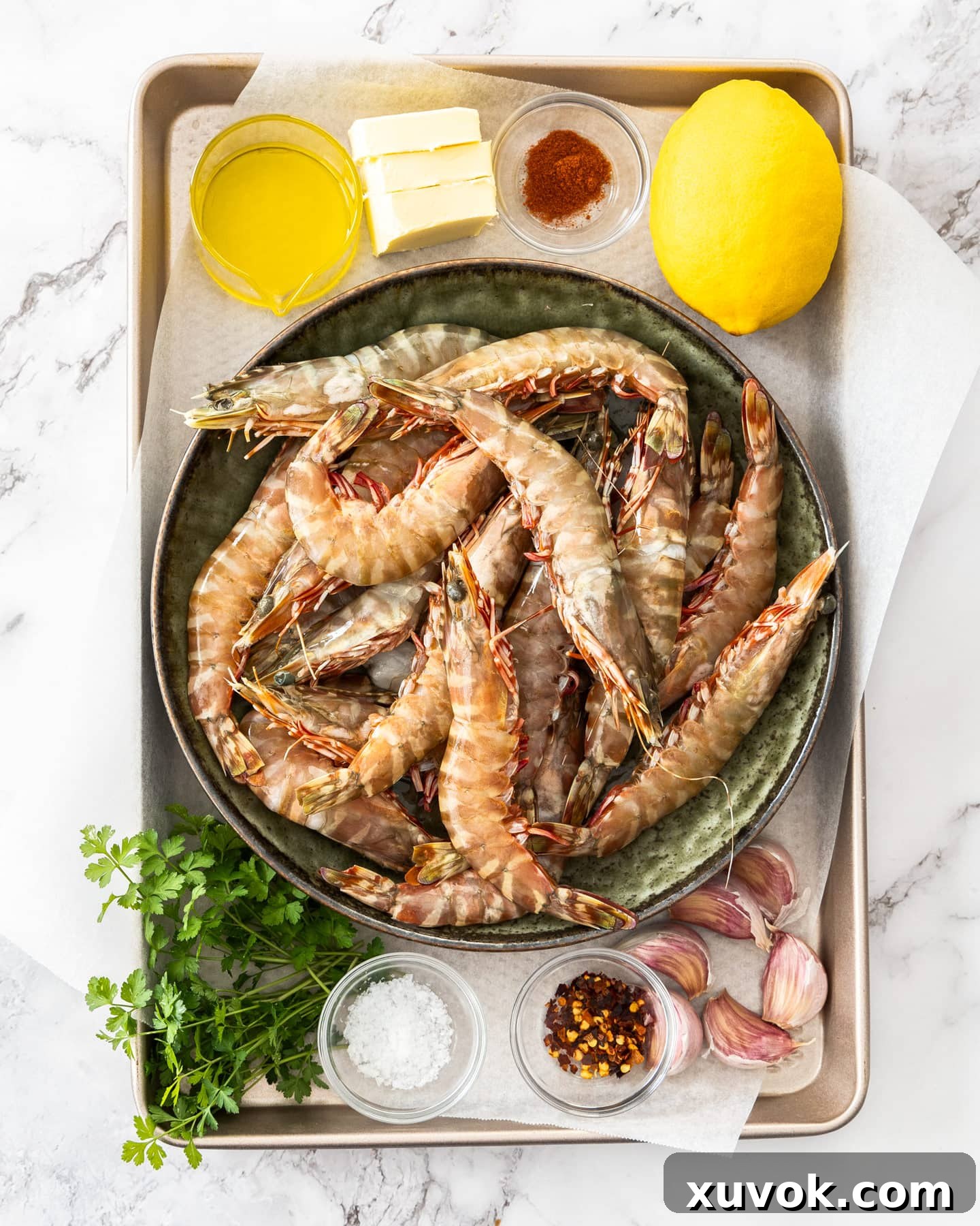 Raw ingredients for garlic prawns laid out on a baking tray, including prawns, garlic, lemon, butter, and spices.