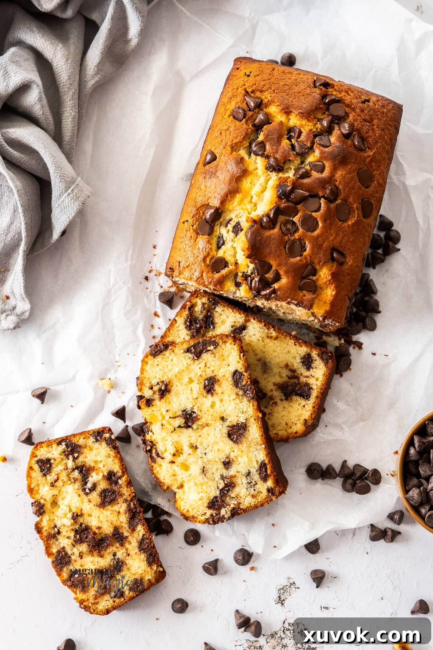 A beautiful chocolate chip loaf cake, half-sliced to reveal its moist interior and generous distribution of chocolate chips, resting on a wire rack.