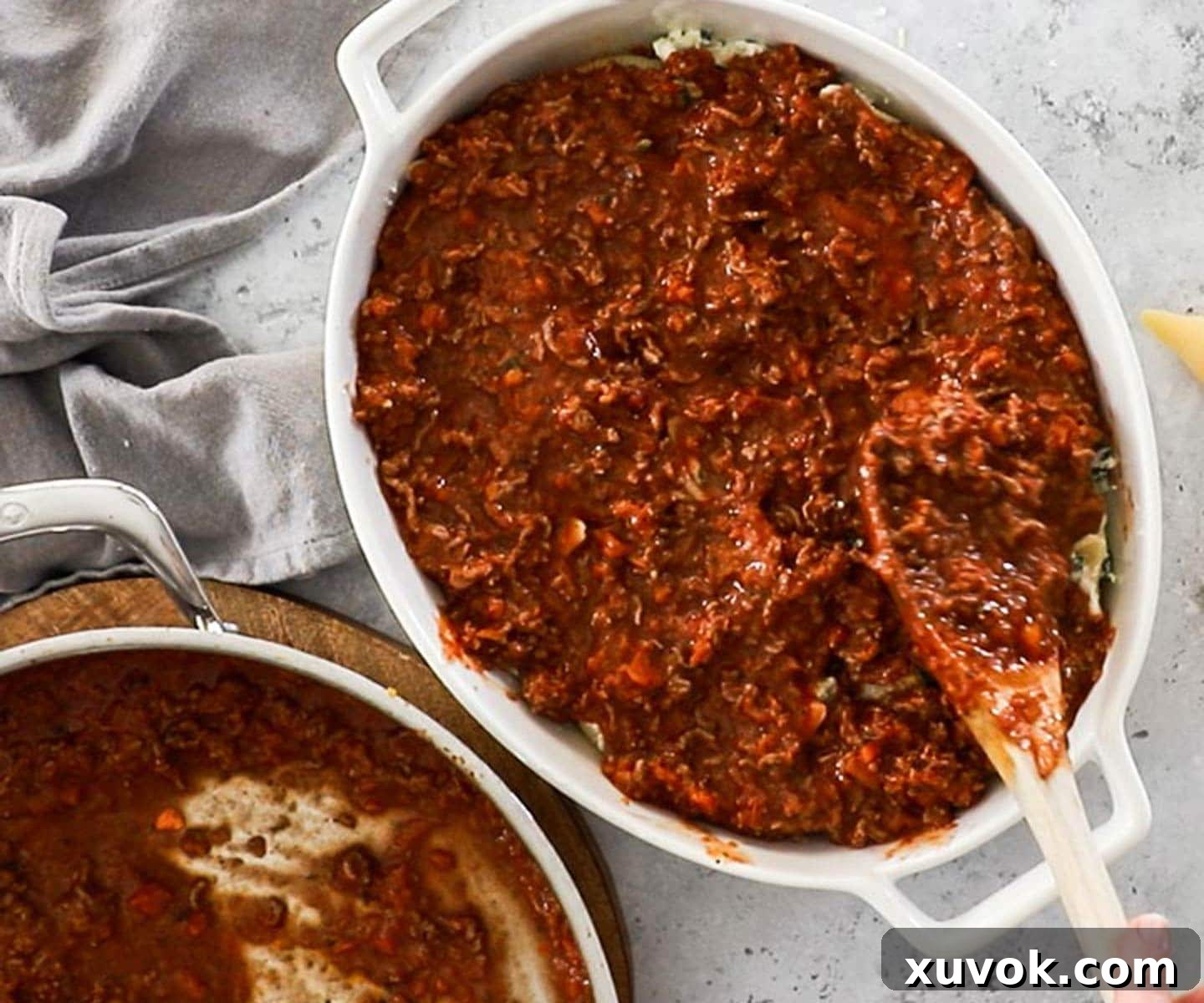 The meat sauce being spread over the stuffed shells.