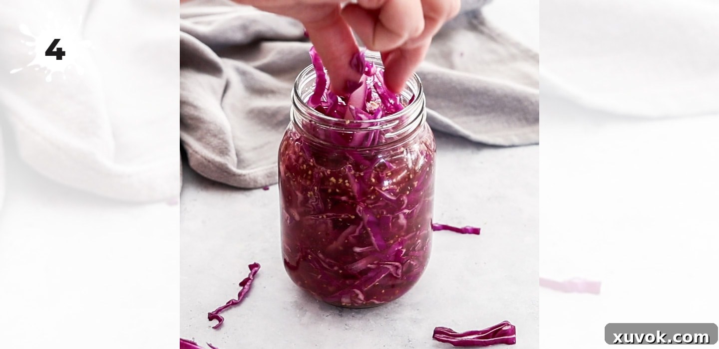 A hand adding sliced red cabbage into a mason jar containing pickling liquid.