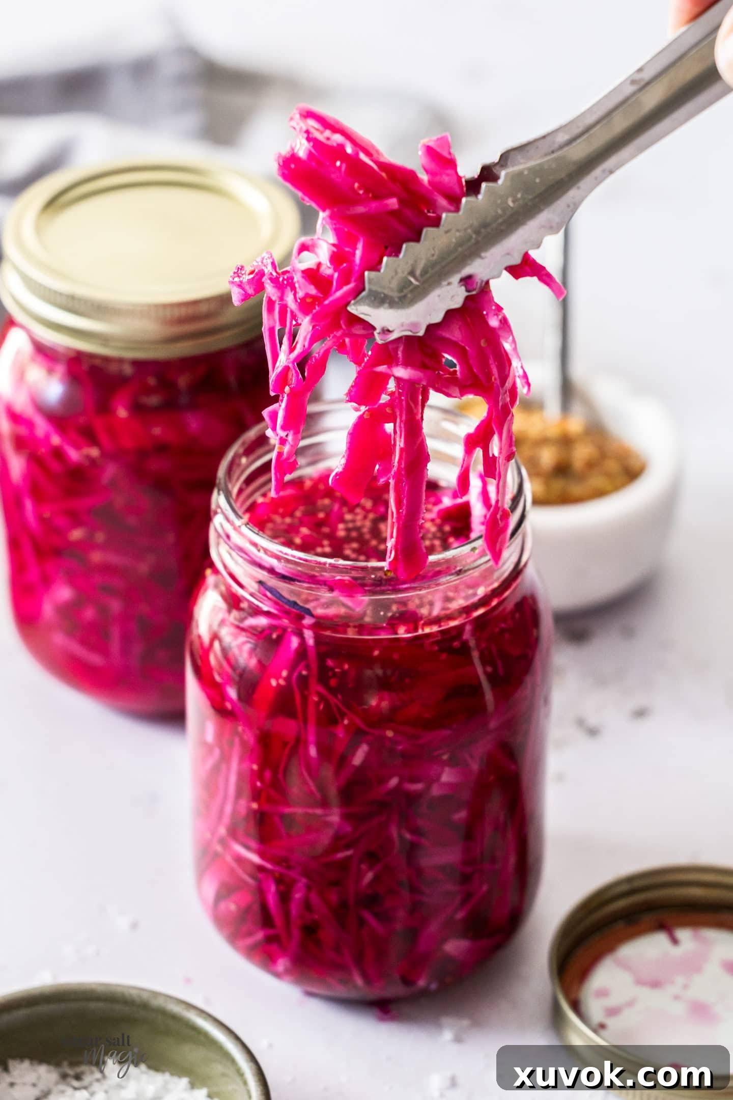 Tongs gently taking a portion of pickled red cabbage out of a glass jar.