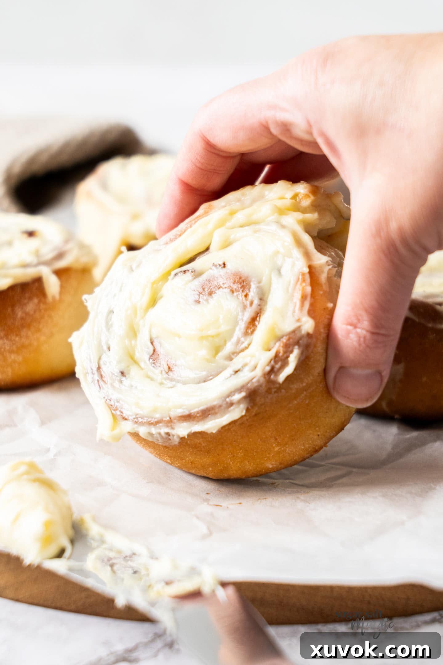 A hand holding a perfectly frosted small batch cinnamon roll, ready to be enjoyed.