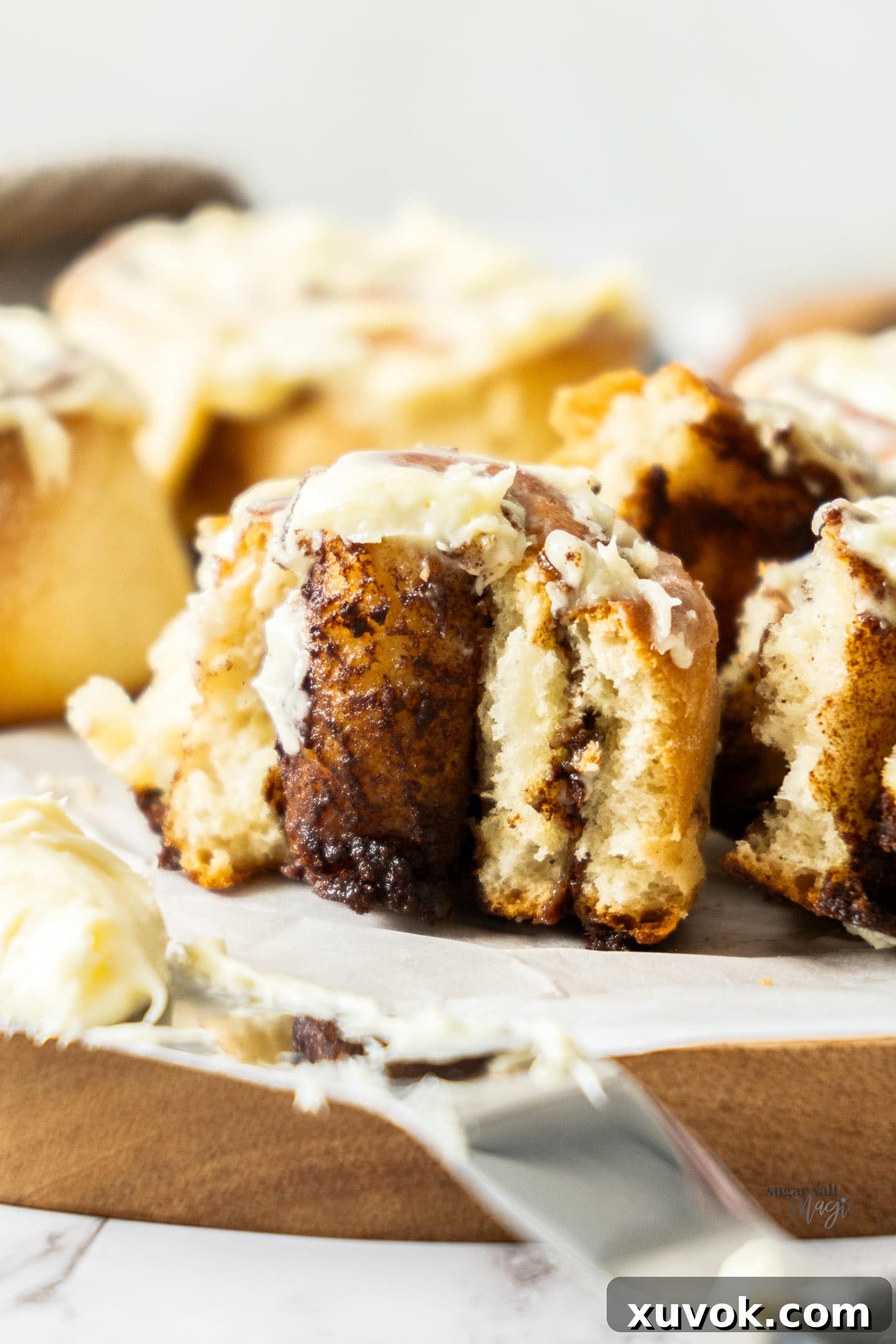 A cinnamon roll torn open, revealing its fluffy interior, distinct cinnamon swirls, and melting cream cheese frosting.