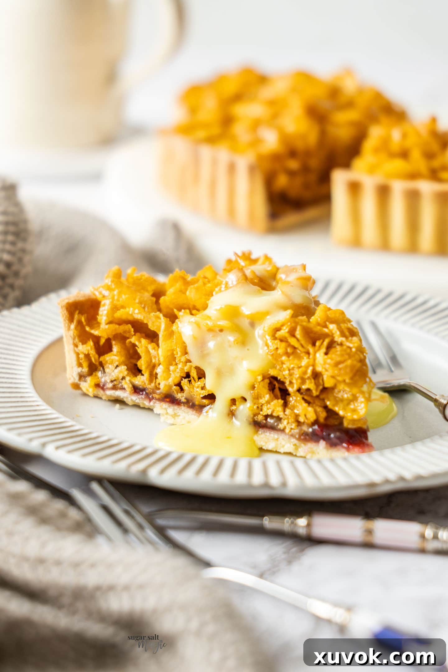 A tantalizing slice of Cornflake Tart served on a white plate, with a river of creamy custard cascading down its side, ready to be enjoyed.