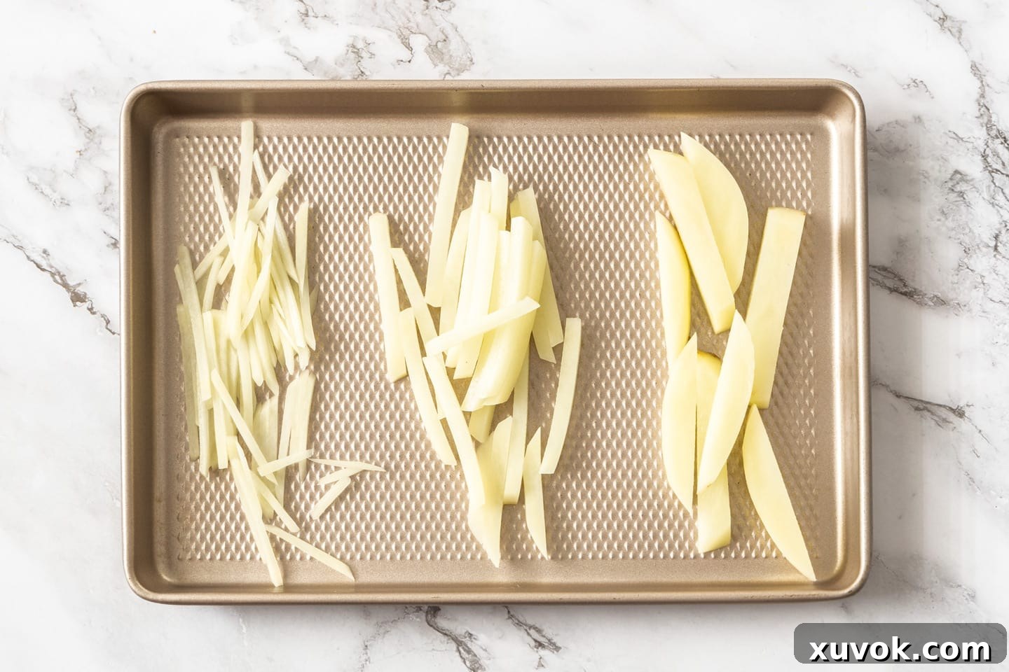 A comparative display of three potato cuts on a tray: thin shoestring fries on the left, standard french fries in the middle, and thick potato wedges on the right, illustrating their distinct sizes.
