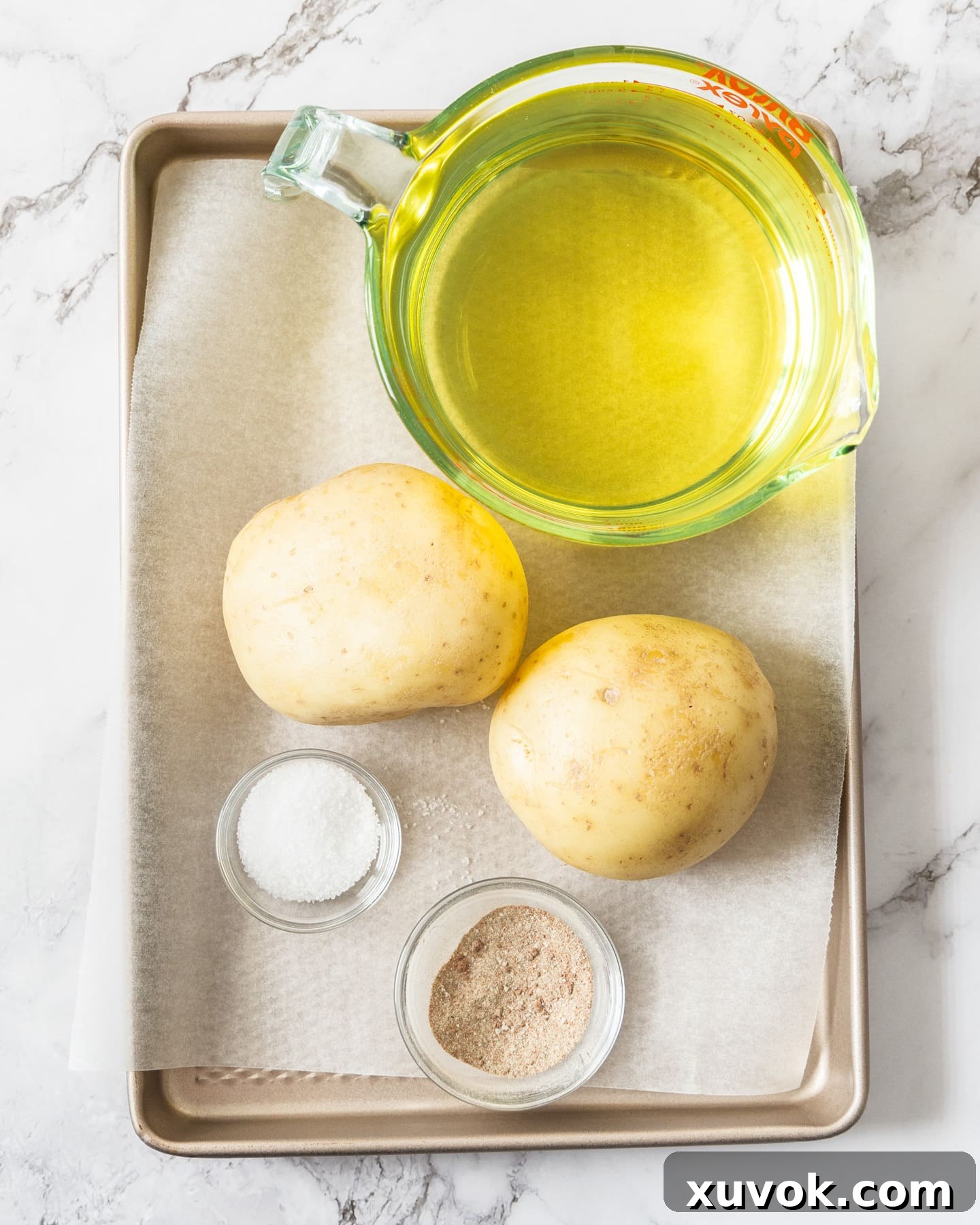 A collection of fresh ingredients laid out: raw potatoes, a bottle of vegetable oil, and a small bowl of mixed seasoning for shoestring fries.