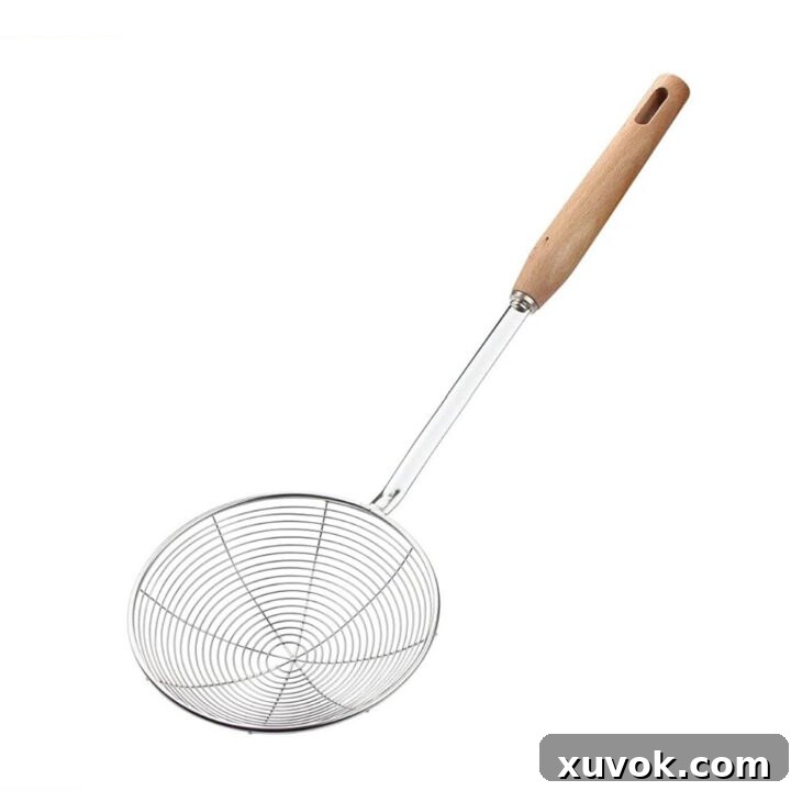 A large wire skimmer with a wooden handle, ideal for safely lowering and removing food from hot oil during deep frying.