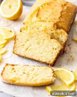 Slices of golden lemon drizzle cake artfully stacked against the remaining loaf, highlighting the moist interior and zesty glaze.