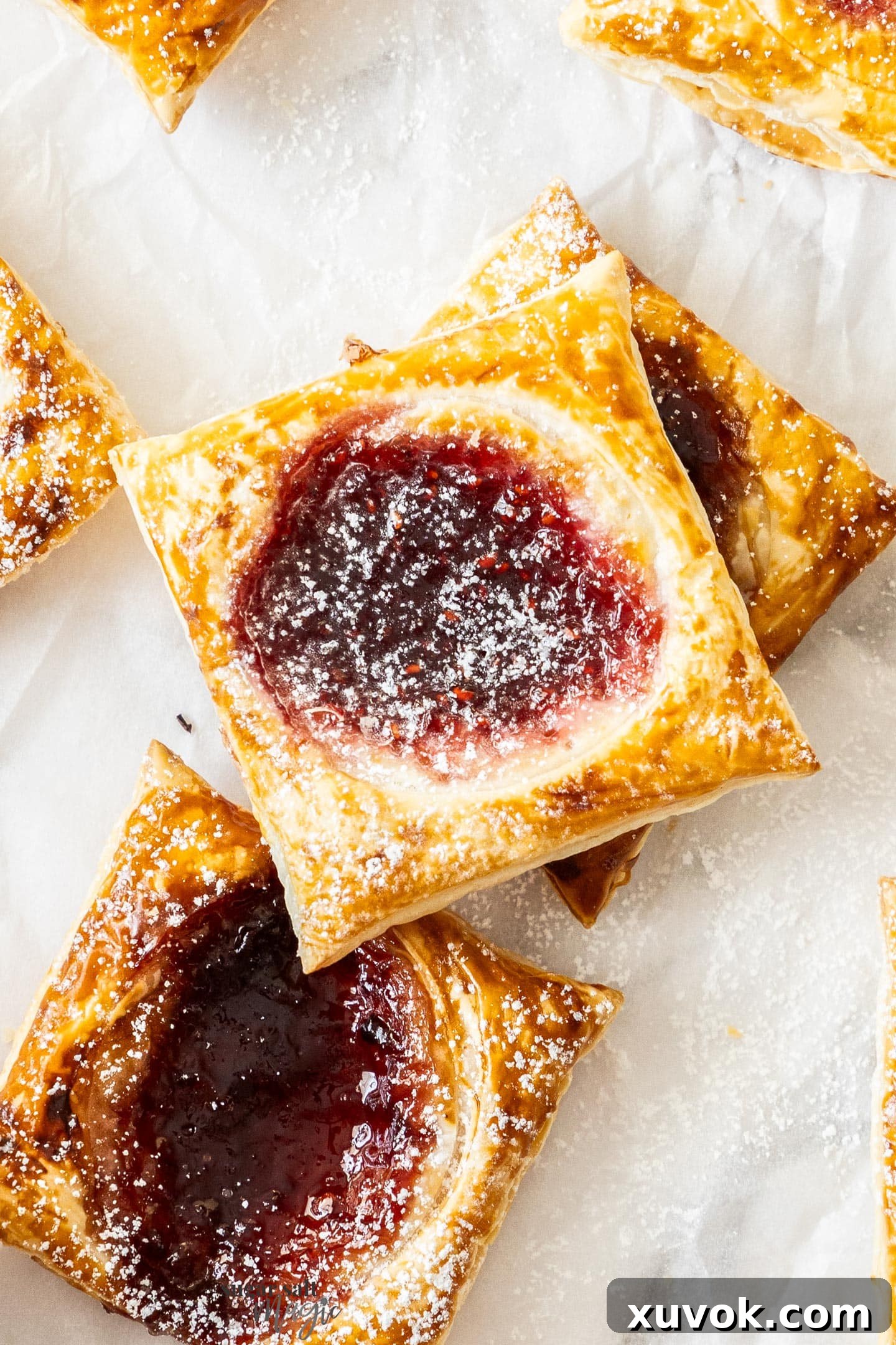 Top down view of freshly baked, golden brown jam puff pastry tarts dusted with powdered sugar, arranged on a baking sheet.