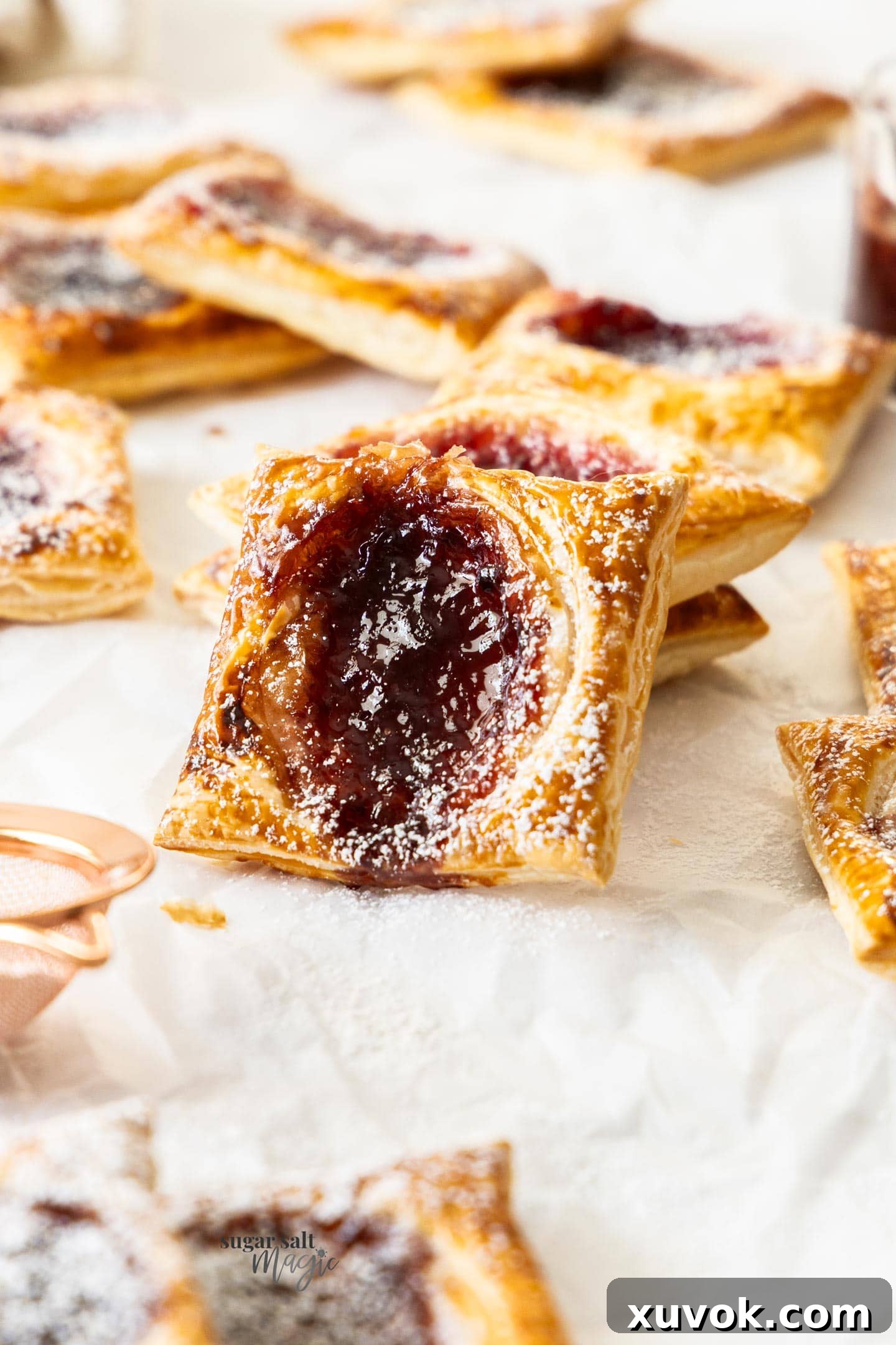 A single puff pastry jam tart, golden brown and jammy, leaning against a stack of similar tarts.