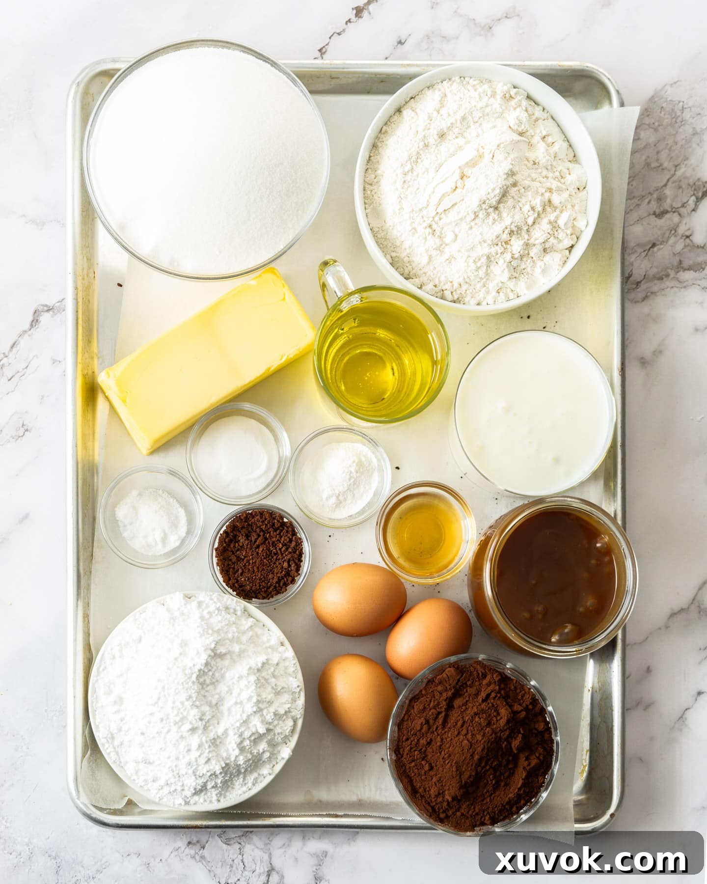 All the essential baking ingredients for a rich chocolate salted caramel cake, neatly laid out on a baking tray, ready for mixing.