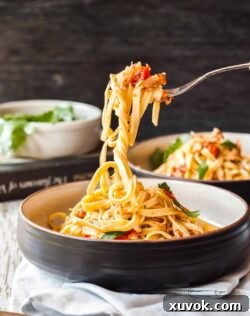 A fork lifting crab linguine out of a black bowl.