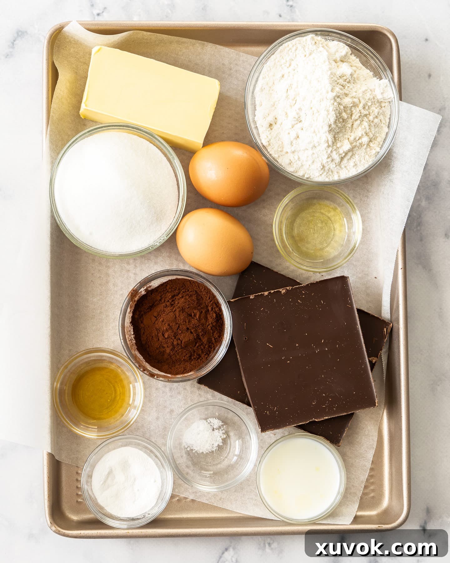 Various ingredients for chocolate madeleines, including flour, cocoa, eggs, and butter, laid out on a baking tray.