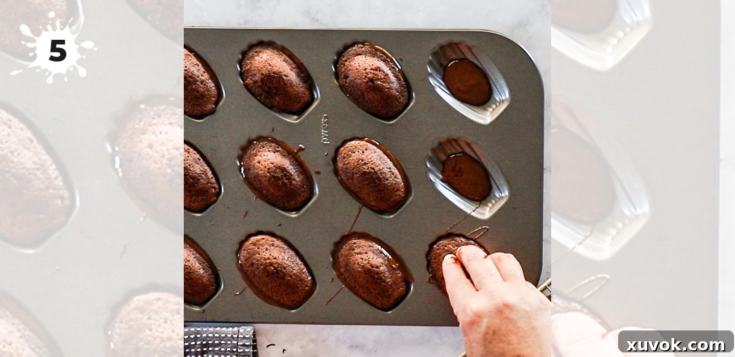 Pressing chocolate madeleines into melted chocolate in a shell-shaped mold.
